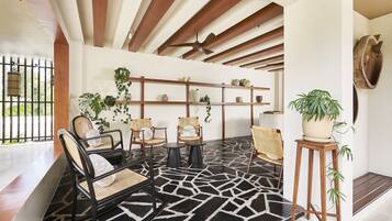 A modern interior with a geometric black and white tiled floor, wooden ceiling beams, wicker furniture, and potted plants.