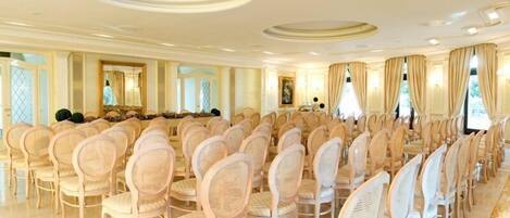 A formal banquet hall with rows of wicker chairs and a long table.