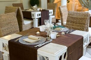 Una mesa de comedor dispuesta con vajilla blanca, incluyendo platos, vasos y cubiertos, en una habitación con sillas de mimbre y una camino de mesa blanca.