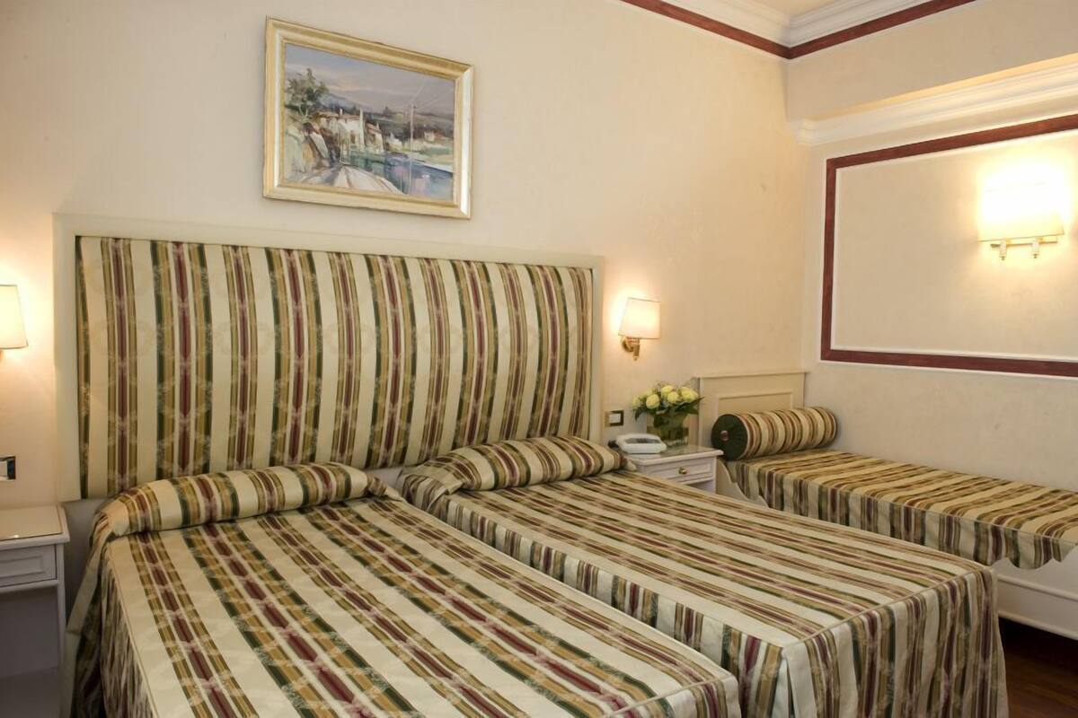 A hotel room with two beds, a painting on the wall, and a bedside lamp.