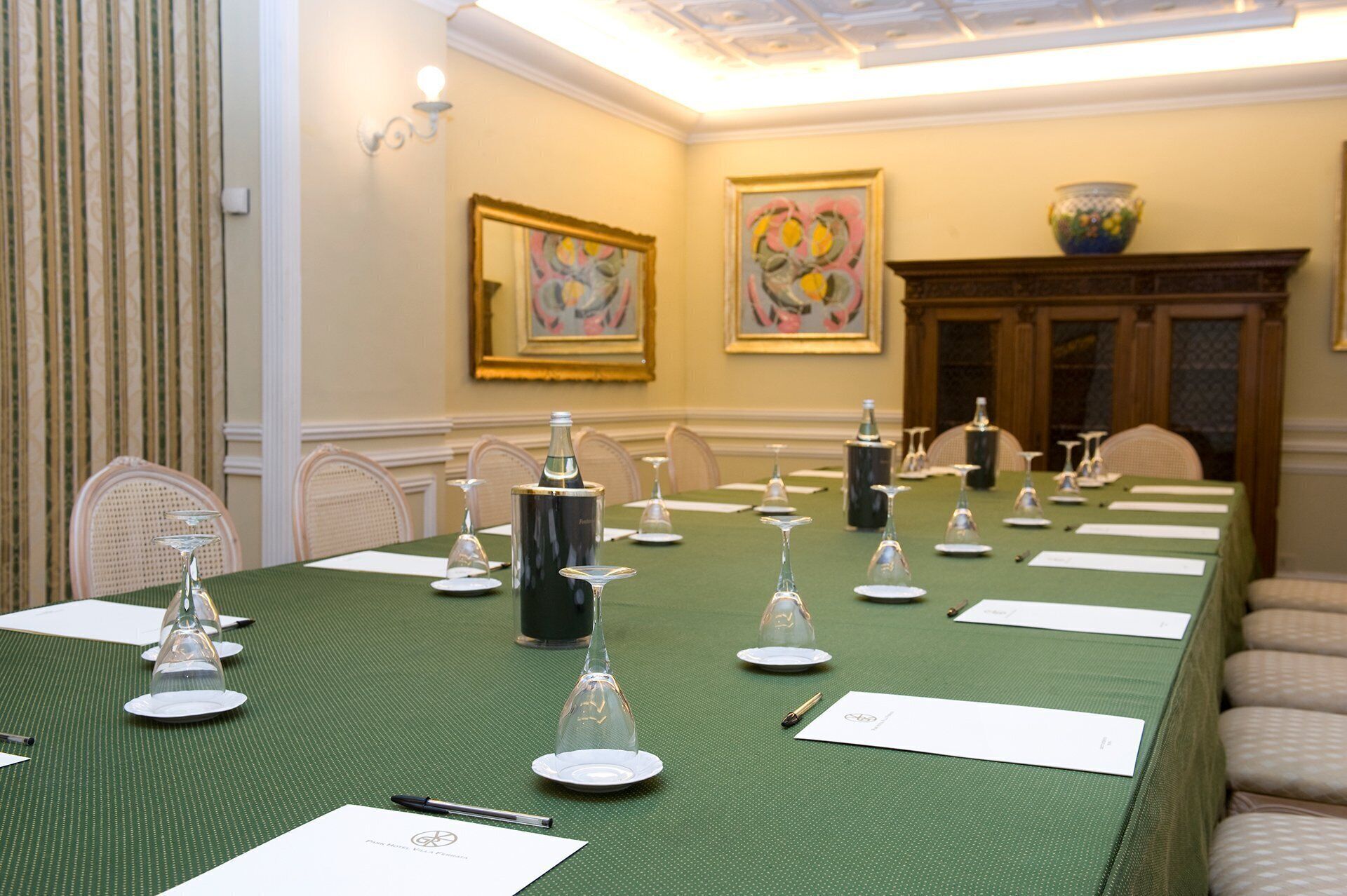 A conference room with a long table set for a meeting, chairs, and framed artwork on the walls.