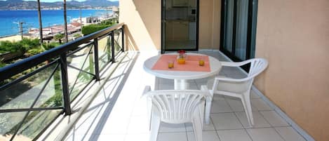 A balcony with a table and chairs, a glass railing, and a view of the sea and mountains.