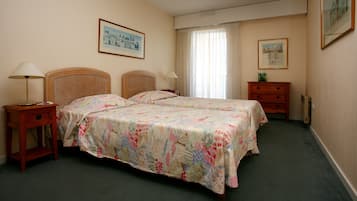 A hotel room with two single beds, a wooden nightstand with a lamp, a dresser, and two framed pictures on the walls.