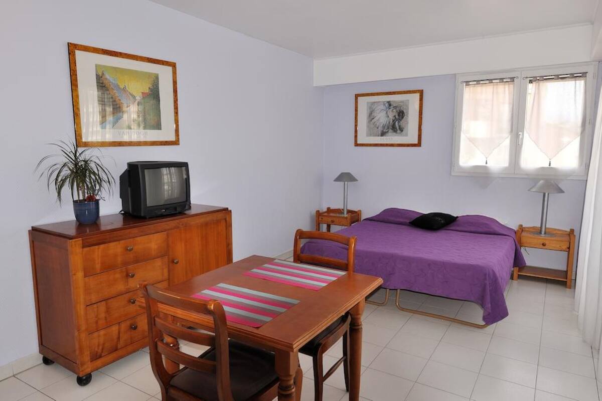 Un dormitorio con una cama, un escritorio con silla, un televisor, una lámpara y dos cuadros en la pared.