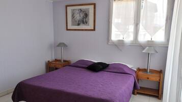 A bedroom with a bed, a nightstand, a lamp, a window with curtains, and a framed picture on the wall.