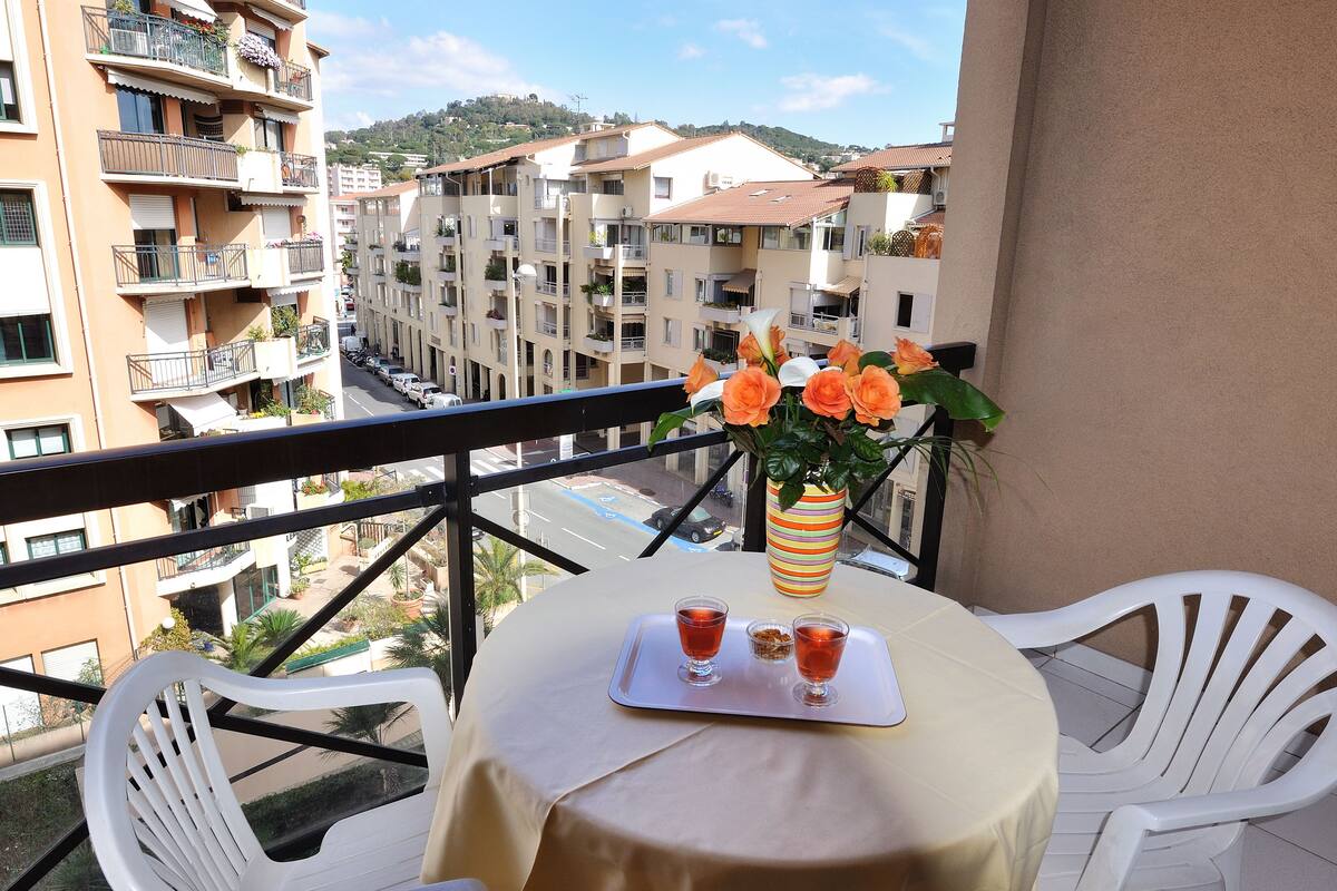 Un balcón con una mesa dispuesta para dos, un florero con flores y vistas a una zona residencial.