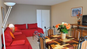 Una habitación con un sofá rojo, una mesa de comedor con sillas, un televisor y una puerta.