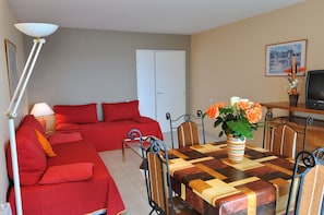 A room with a red sofa, a wooden dining table with chairs, a TV, and a lamp. - Residhotel Villa Maupassant (Cannes)