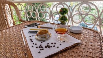A wicker table with a white cloth, a cup of tea, a glass of amber liquid, a small potted plant, and scattered coffee beans.