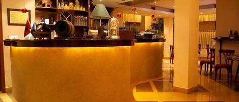 A hotel lobby with a curved reception desk, a bar area with bottles, and a dining area with chairs.