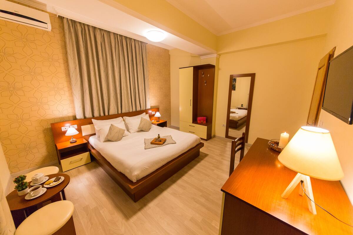 A hotel room with a bed, bedside tables, a desk, a chair, a mirror, and a small table with a candle.