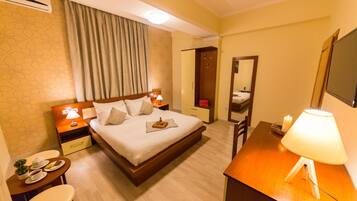 Habitación de hotel con cama, mesitas de noche, escritorio, silla, espejo y una pequeña mesa con una vela.