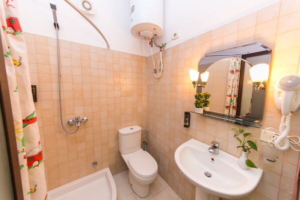 Un baño con inodoro, lavamanos, ducha y espejo con luces.