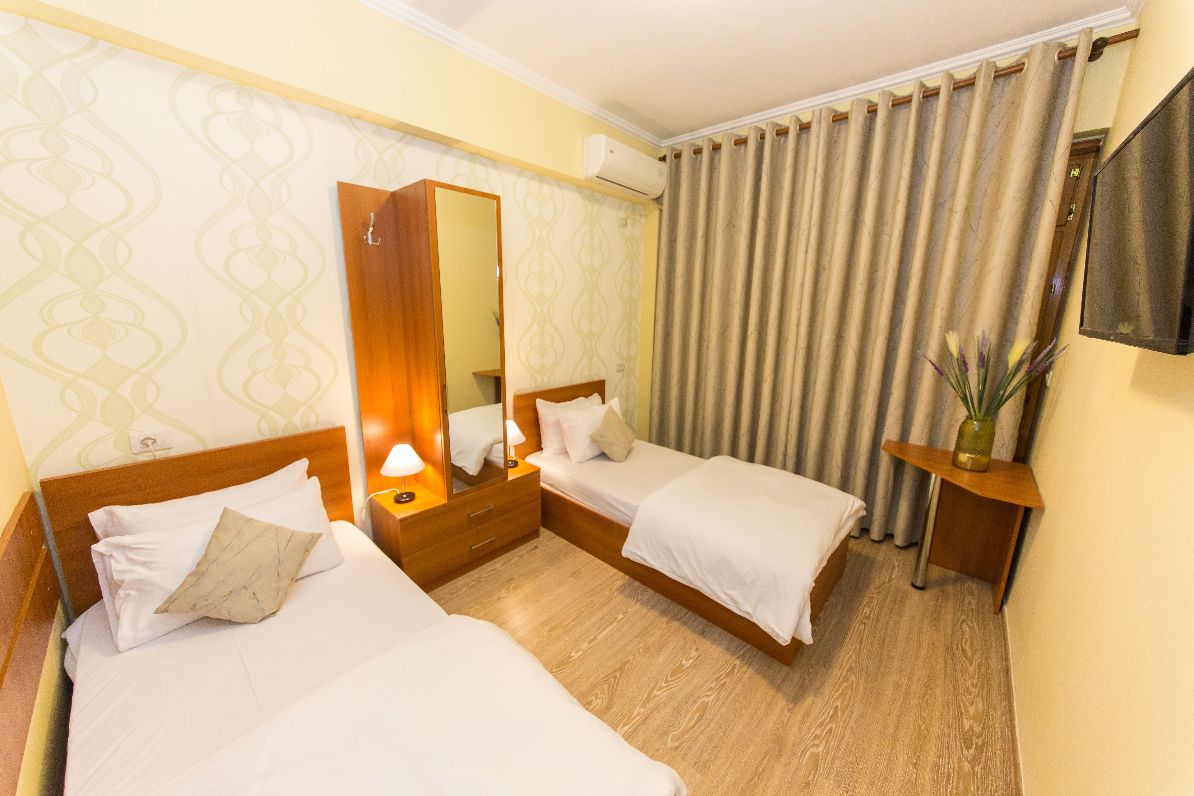 Une chambre d’hôtel avec deux lits, un miroir, une table de chevet avec une lampe, une télévision et un rideau.