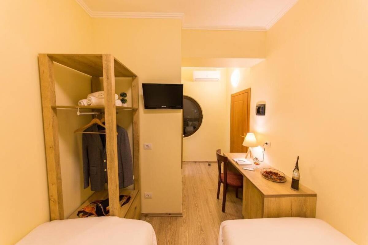 A hotel room with a wooden wardrobe, a desk with a lamp, a television, and a bed.