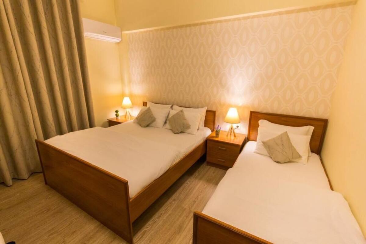 A hotel room with two beds, a patterned wallpaper, and an air conditioning unit.