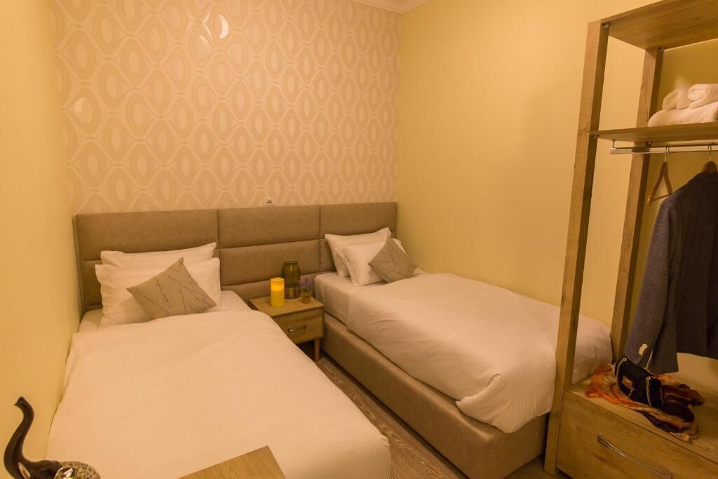 Una habitación de hotel con dos camas individuales, una mesita de noche con lámpara, un espejo y un armario.