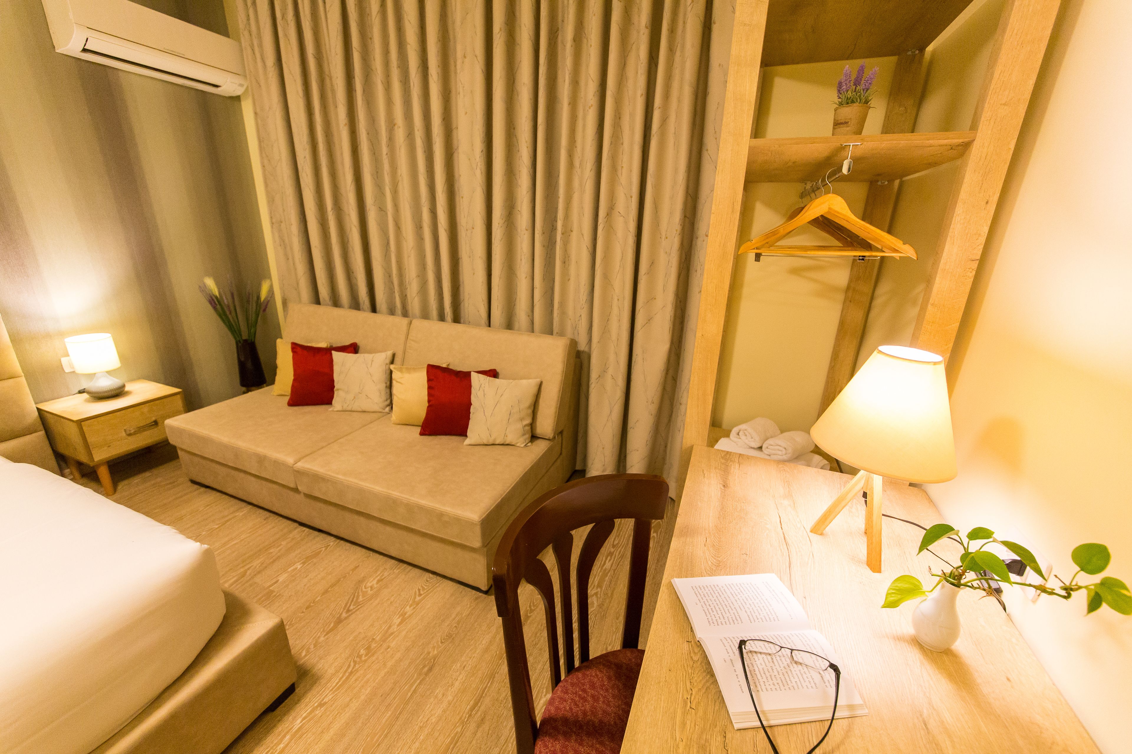 Una habitación de hotel con cama, sofá, escritorio con lámpara, una silla y una planta colgante.