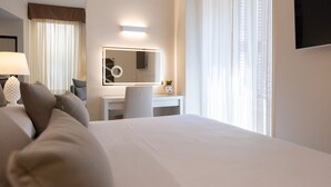 A hotel room with a large bed, a desk with a chair, a mirror, and a TV on the wall. - Relais Piazza Del Popolo - Aminta Collection Luxury Rooms (Rome)