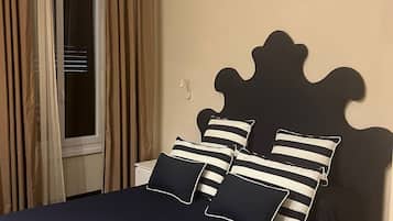 A bed with a dark blue bedspread and striped pillows, a window with curtains, and a wall-mounted light fixture.