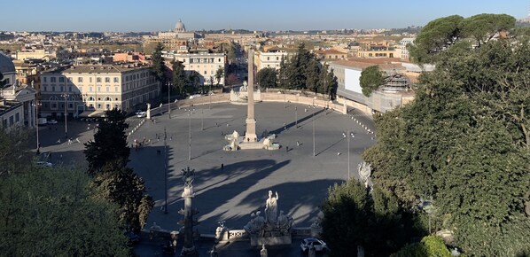 Una amplia plaza con un monumento central, rodeada de arquitectura clásica y árboles.
