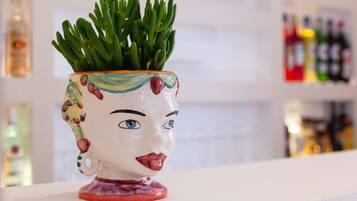 A ceramic pot with a face design, containing green plants, placed on a white surface.