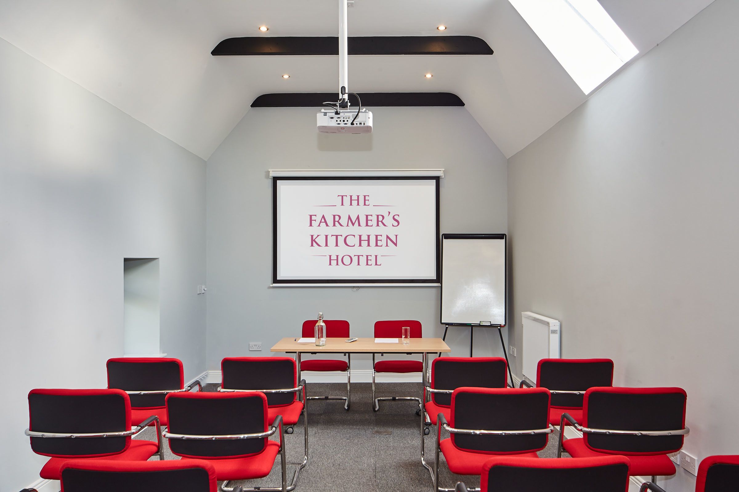 Ein Konferenzraum mit Projektionsfläche, die "The Farmer's Kitchen Hotel" zeigt, und einer Whiteboard-Tafel.