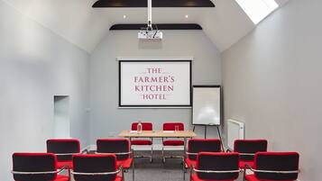 Ein Konferenzraum mit Projektionsfläche, die "The Farmer's Kitchen Hotel" zeigt, und einer Whiteboard-Tafel.