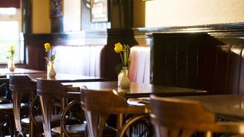 A restaurant interior with wooden tables and chairs, a vase with yellow flowers, and a cushioned bench.