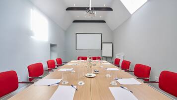 Una sala de conferencias con una larga mesa, sillas rojas, un proyector y una pizarra.