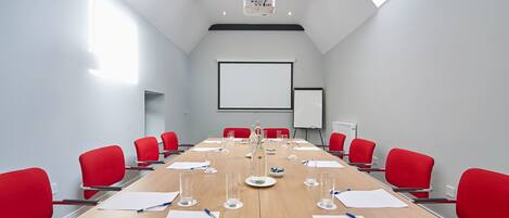 A conference room with a long table, red chairs, a projector, and a whiteboard.