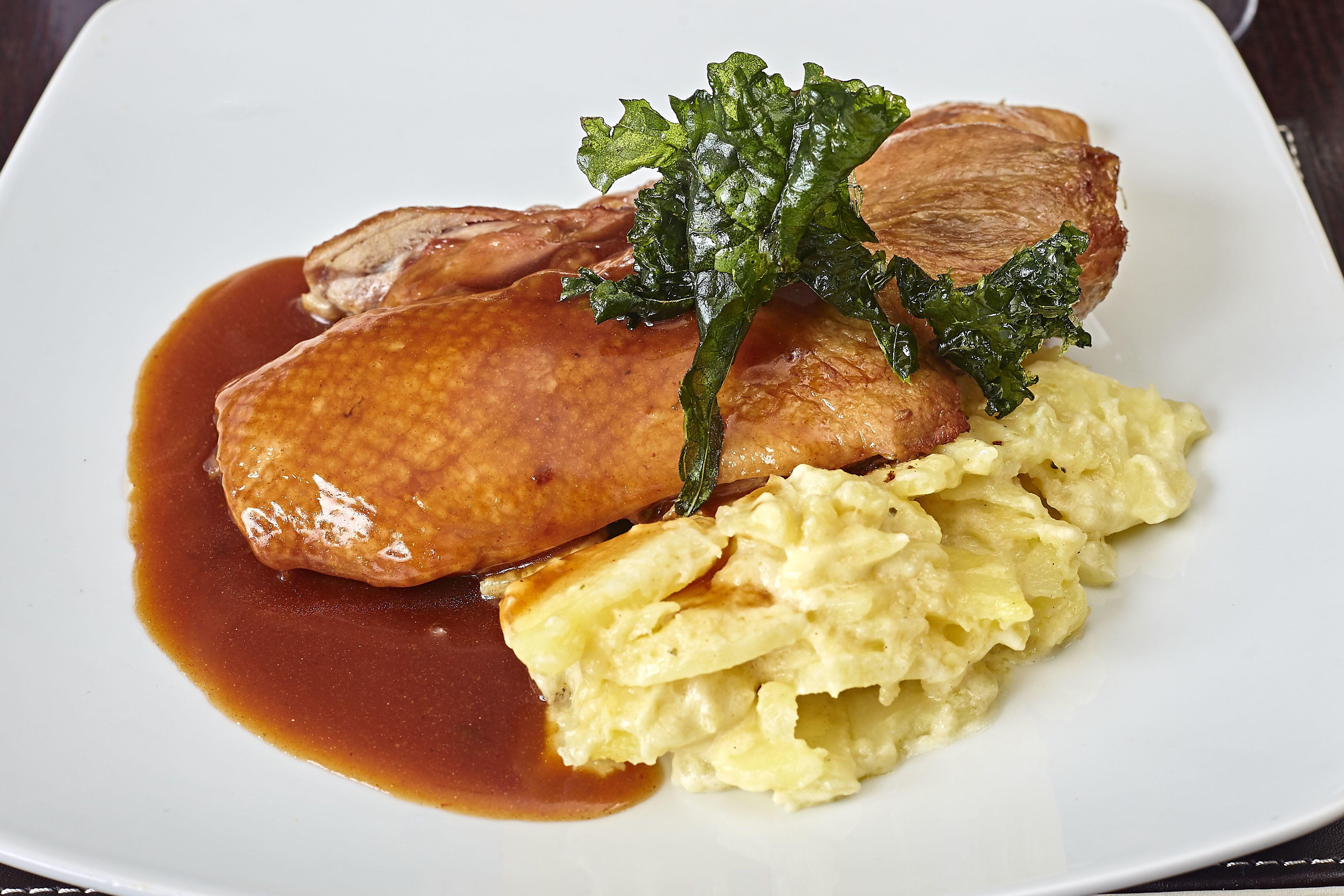 Une assiette contenant un morceau de viande, de la purée de pommes de terre et une garniture de légumes verts.