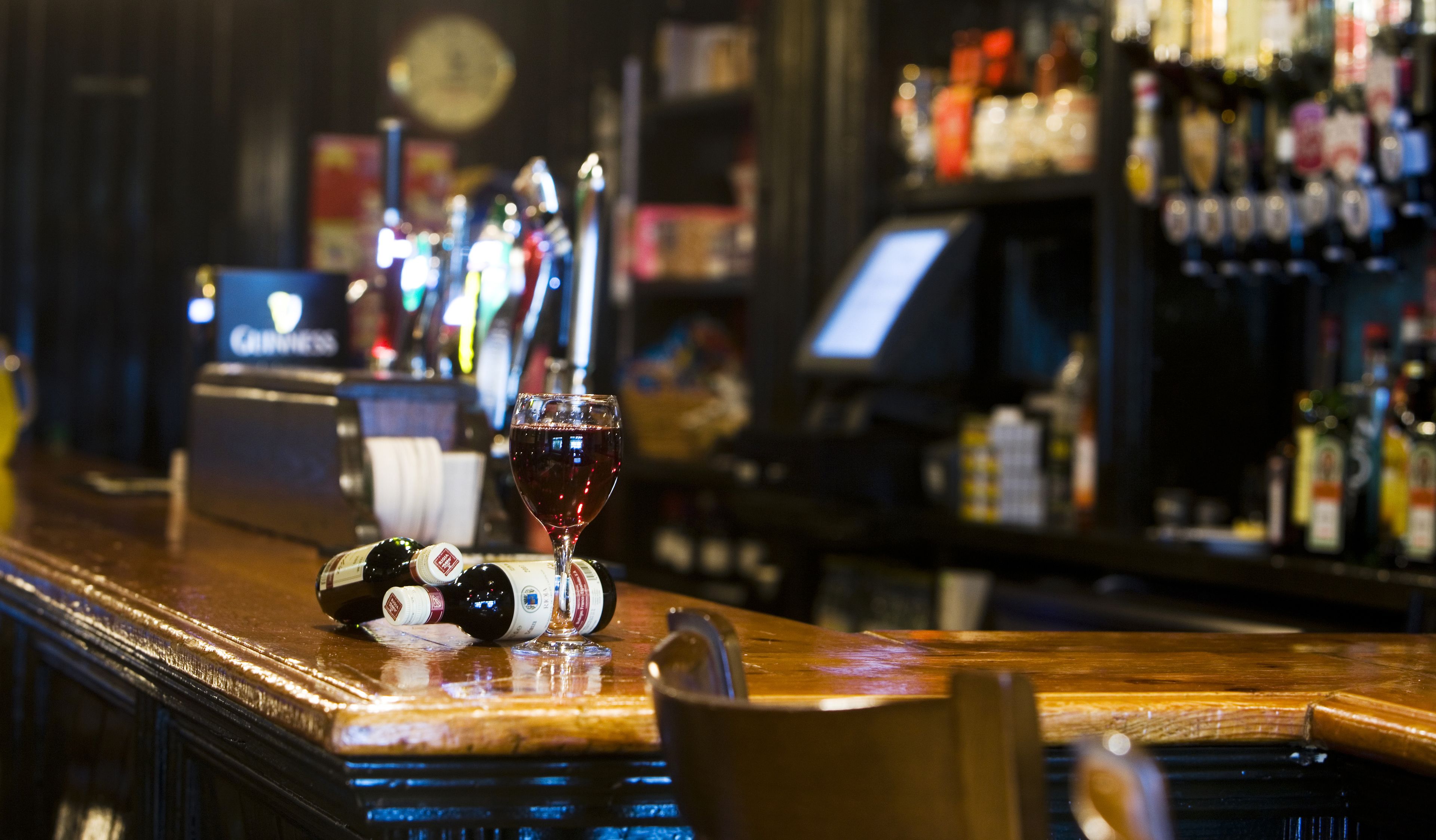 Een bar met een glas rode wijn, flessen en een biertappunt.
