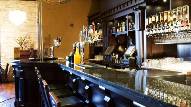 Una zona de bar con una barra alargada, diversas opciones de asientos y una variedad de botellas y vasos en estantes.