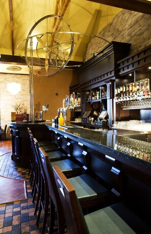 Una zona de bar con una barra alargada, diversas opciones de asientos y una variedad de botellas y vasos en estantes.