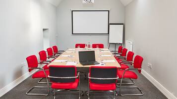 A conference room with a long table, red chairs, a projector, and a whiteboard.
