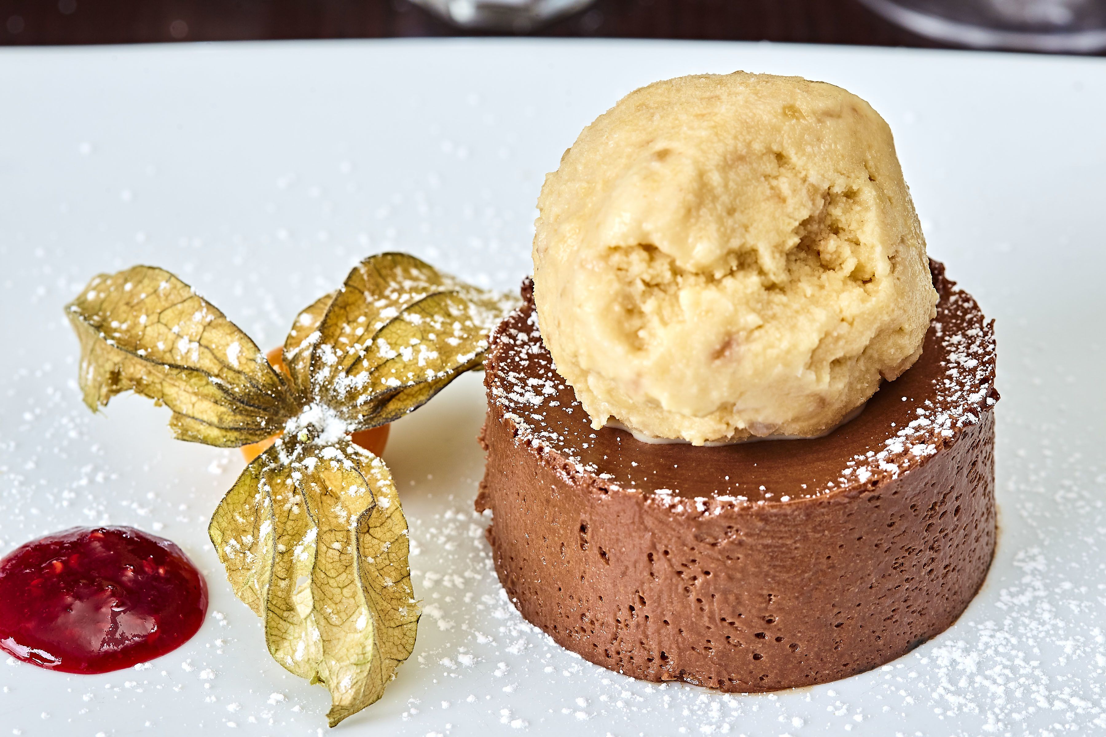 A dessert with a scoop of ice cream on top of a chocolate cake, accompanied by a decorative leaf and a berry sauce.