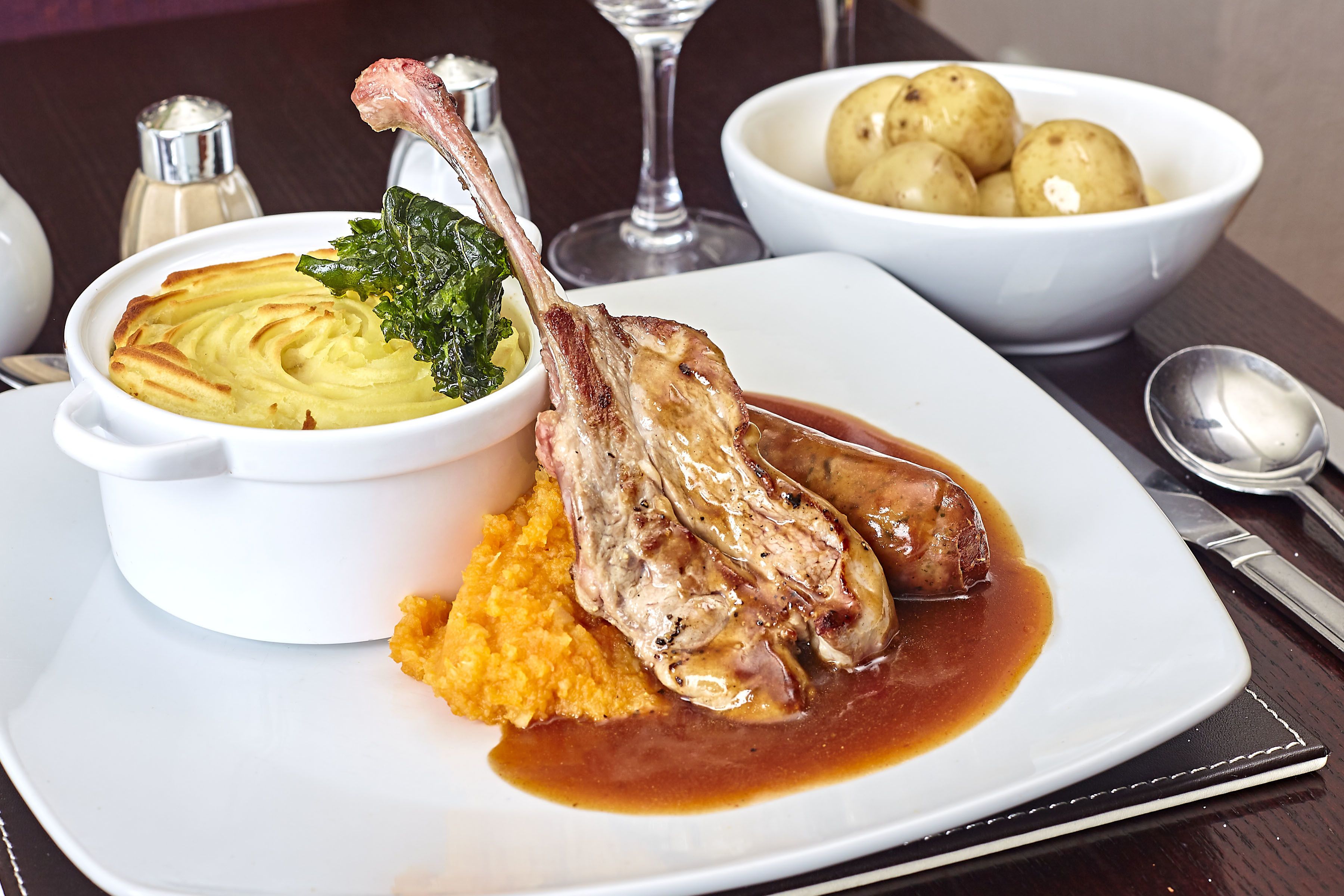 A plate with lamb chops, mashed potatoes, and greens.