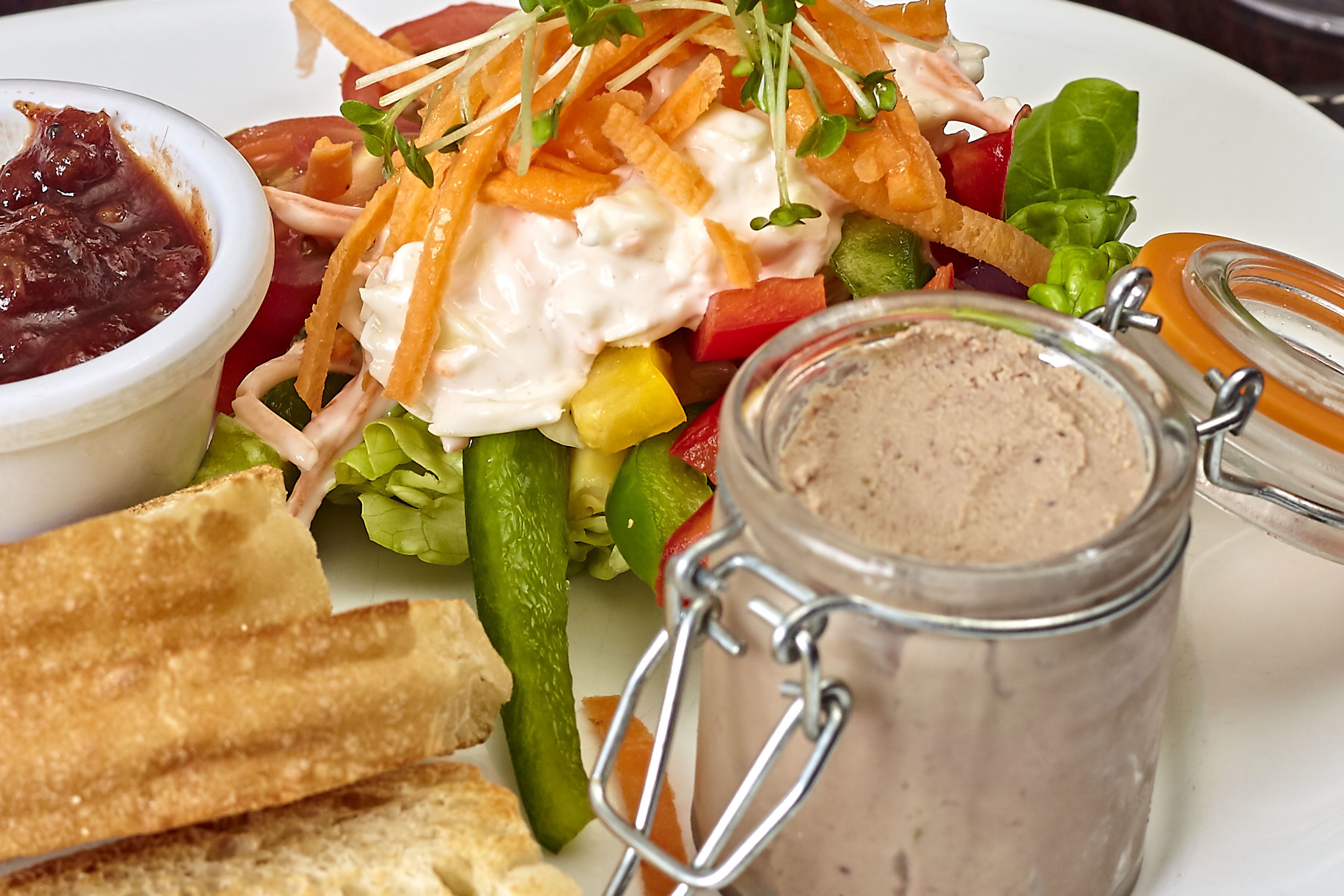 A plate with a salad, a jar of spread, and a bowl of sauce.