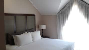 Un dormitorio con una cama grande, una mesita de noche con lámpara, una ventana con cortinas e iluminación en el techo.