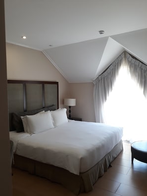 Un dormitorio con una cama grande, una mesita de noche con lámpara, una ventana con cortinas e iluminación en el techo.