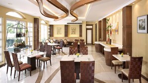 A spacious dining area with multiple tables and chairs, a central bar, and a view of the outdoors. - Hotel Venezia (Legazpi)