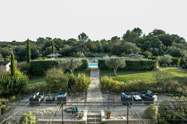 Um jardim com um caminho que leva a uma piscina, cercado por vegetação e área de estar ao ar livre.