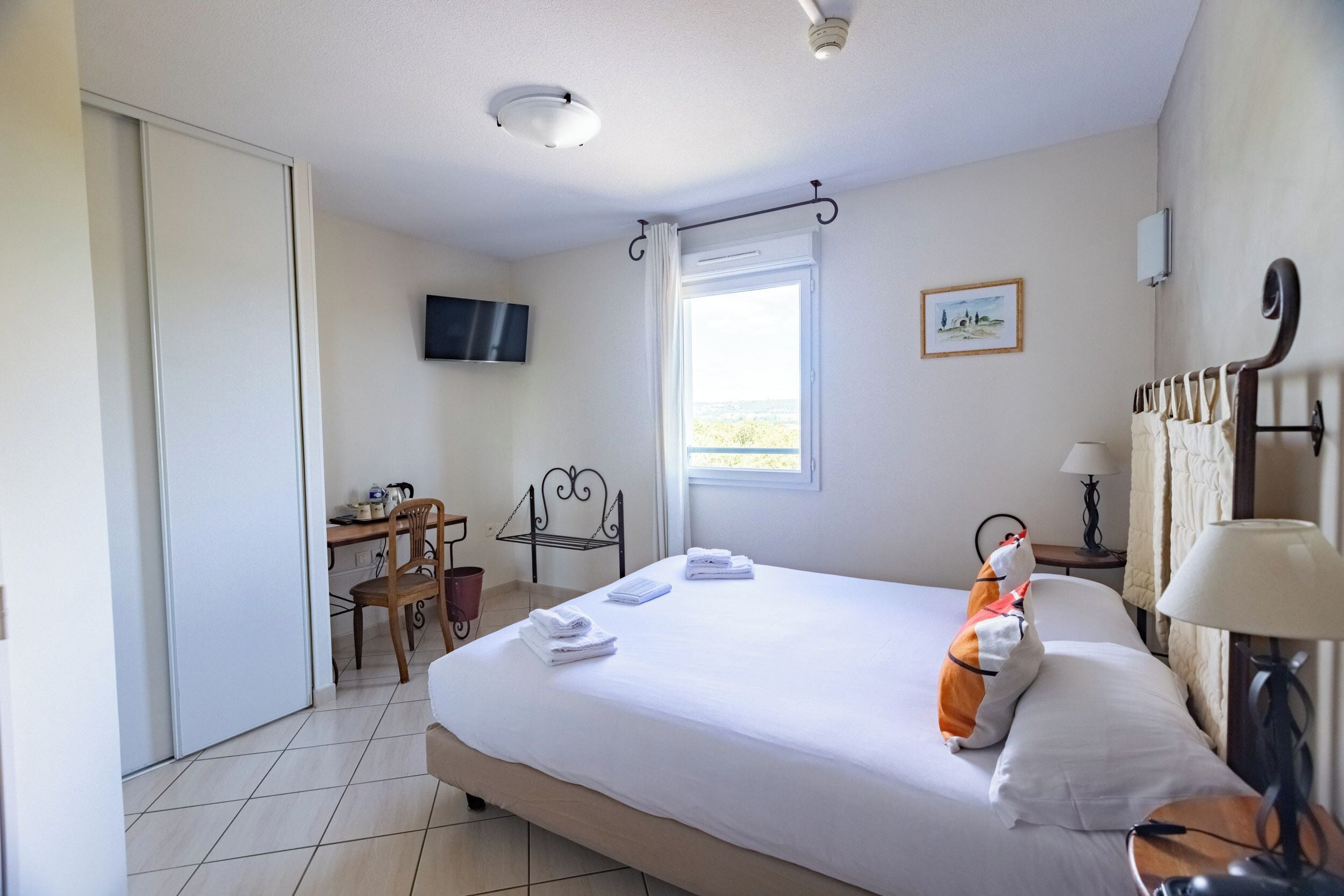 A hotel room with a bed, a desk, a chair, a television, and a window with curtains.