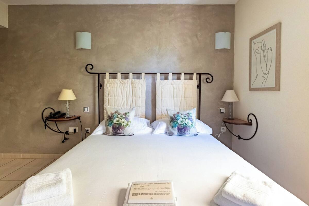 Een net opgemaakt bed met witte lakens, twee nachtkastjes met lampen en decoratieve kussens.