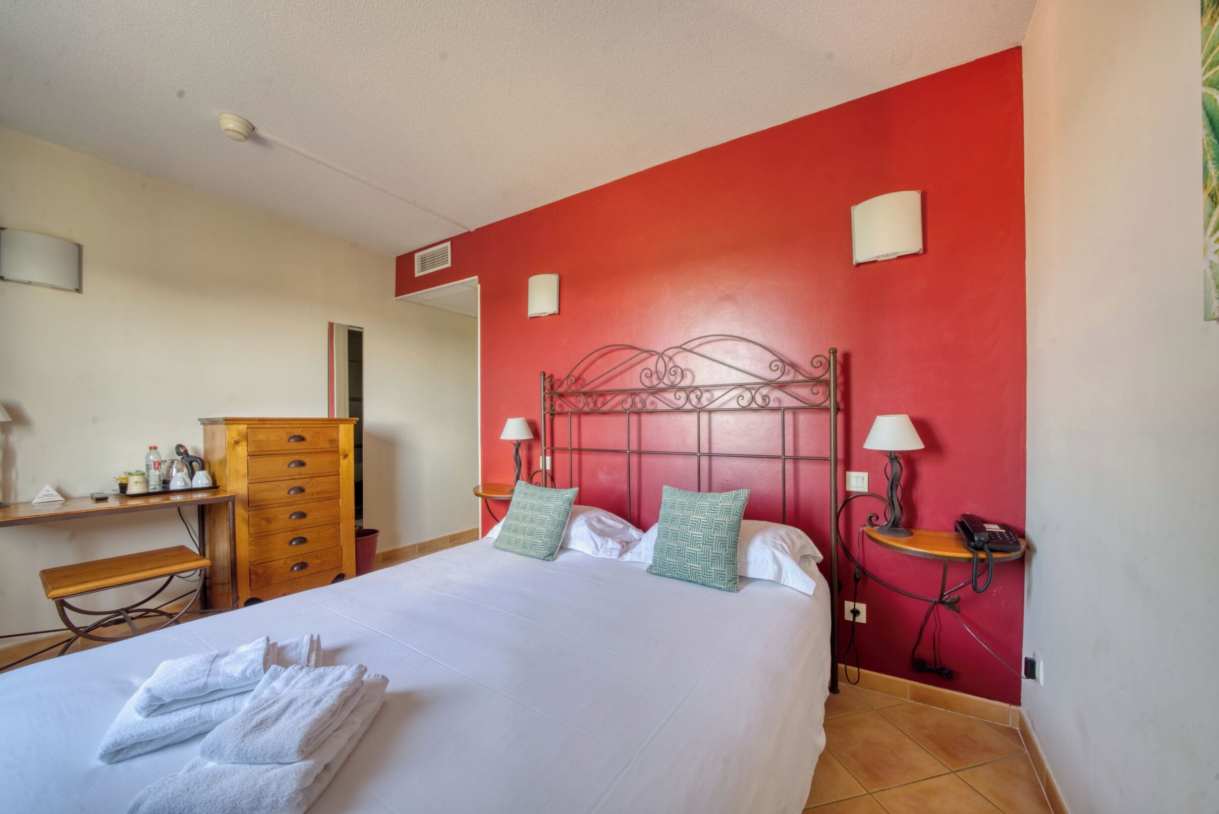 Habitación de hotel con una cama, un tocador de madera, un escritorio con lámpara y una mesita con teléfono.