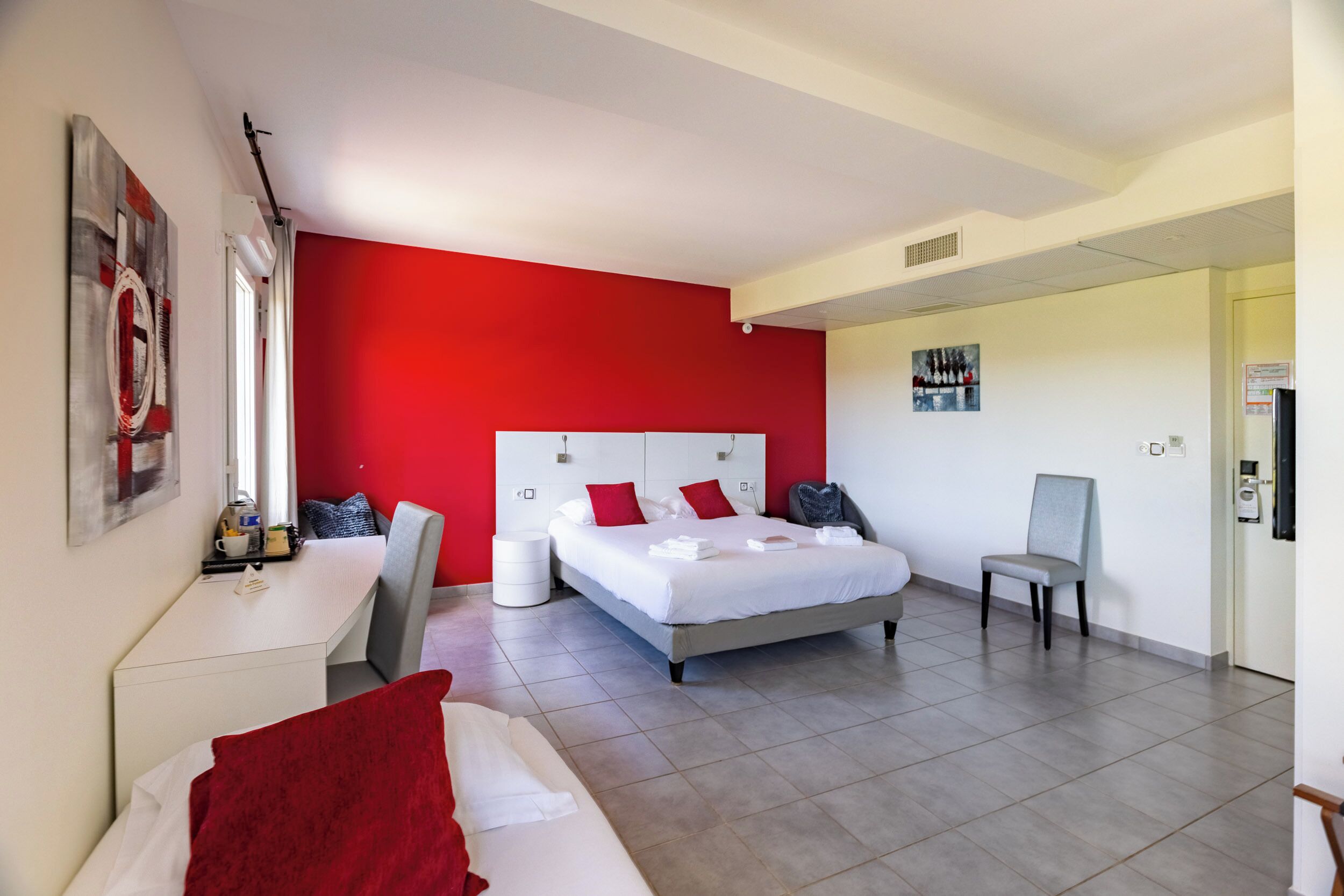 Quarto de hotel com cama, escrivaninha, cadeira e parede decorada em vermelho.