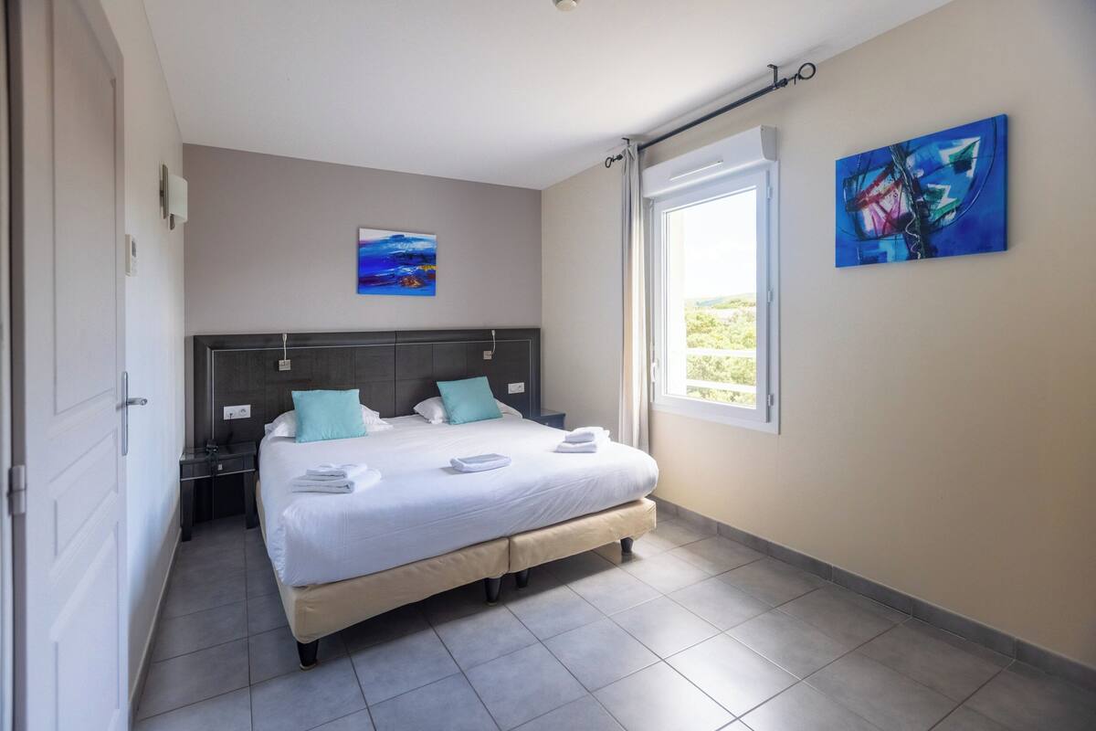 Een slaapkamer met een bed, nachtkastjes, een raam en twee schilderijen aan de wand.