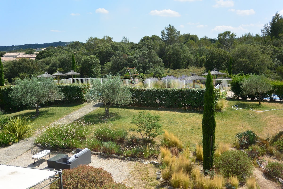 Un jardín ajardinado con senderos, una zona de estar y un área de juegos cercada.