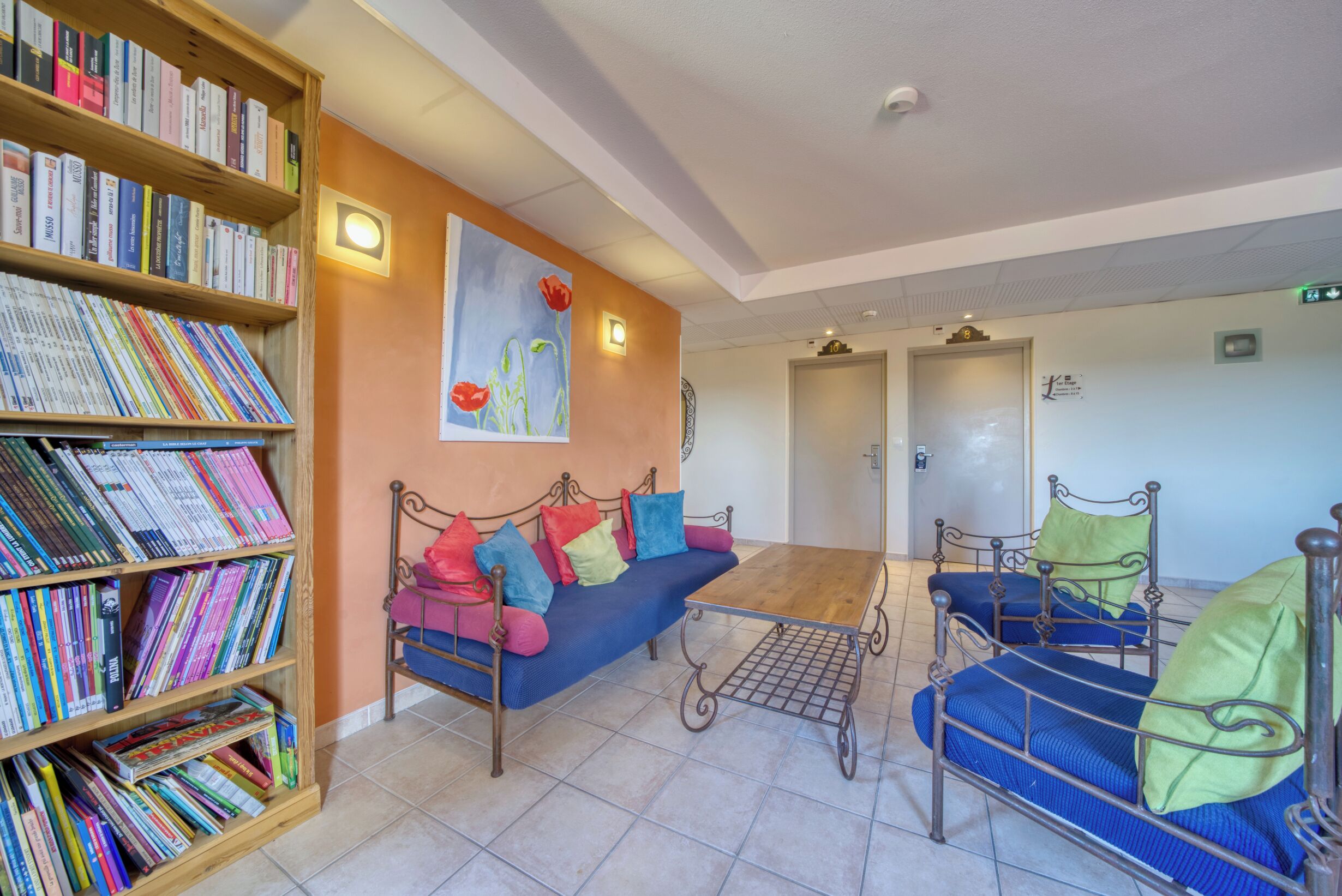 Una habitación con estantería, sofá, estructura de cama metálica y un cuadro en la pared.